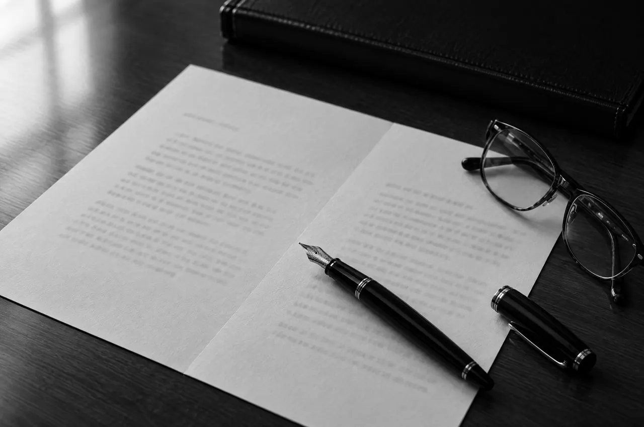 A two-page letter on a walnut desk with a fountain pen and reading glasses