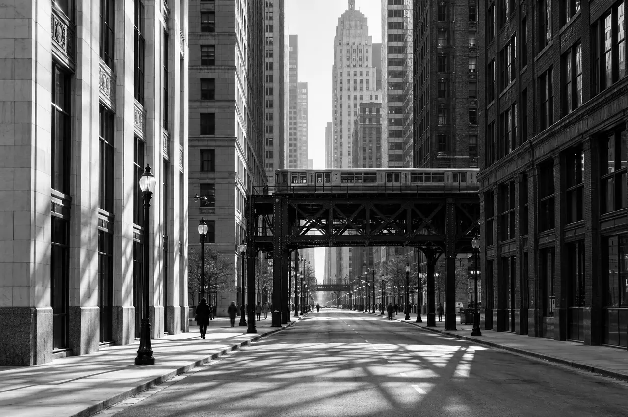 A Loop street lined with limestone and brick office buildings, the elevated train crossing at the end of the block